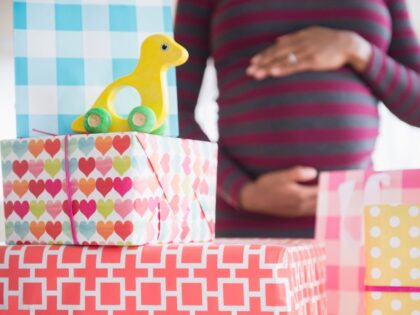 Black pregnant woman admiring gifts at baby shower - stock photo