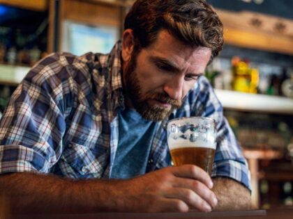 Sad man looking at beer glass while sitting in beer bar