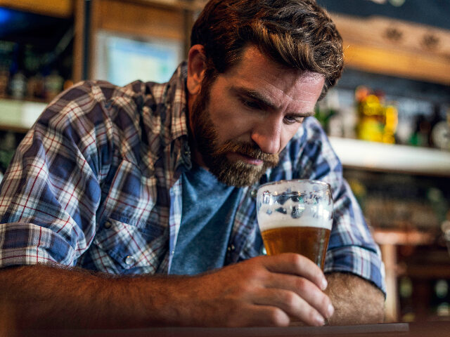 Sad man looking at beer glass while sitting in beer bar