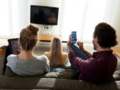 Friends sitting on couch in livingroom, using digital devices