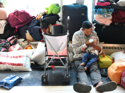 CHICAGO, ILLINOIS - MAY 09: A migrant father from Venezuela feeds his 15-month-old son in the lobby of a police station where they have been staying with other migrant families since their arrival to the city on May 09, 2023 in Chicago, Illinois. Chicago Mayor Lori Lightfoot issued a state …