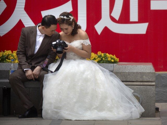 A couple in wedding dress look at photos on the back of a camera near a propaganda slogan