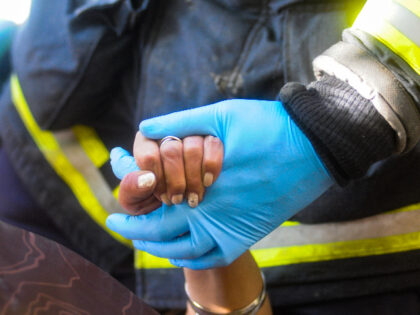 A rescuer's / firefighter's hand holds a victim's hand during simulation.