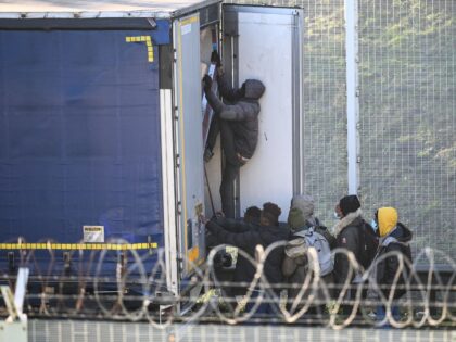 A migrant climbs into the back of lorries bound for Britain while traffic is stopped upon