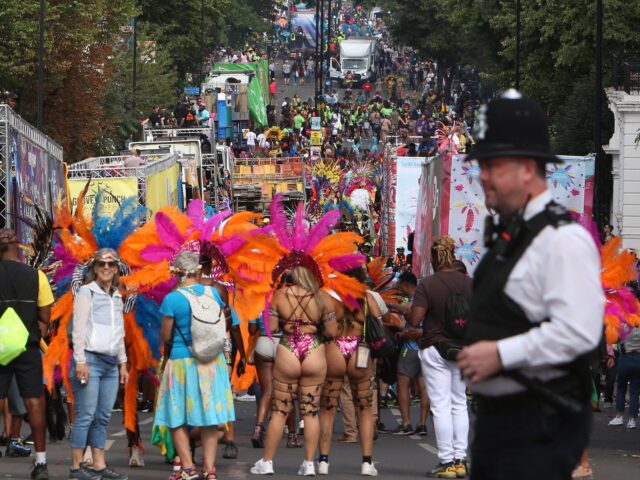 A police officer stands on duty as performers in costume take part in the carnival on the main Parade day of the Notting Hill Carnival in west London on August 29, 2022. - London's Notting Hill carnival celebrates Caribbean culture, at a carnival considered the largest street demonstration in Europe. …