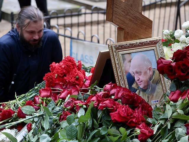 A man sits near the grave of Yevgeny Prigozhin, who died in a plane crash, as people visit