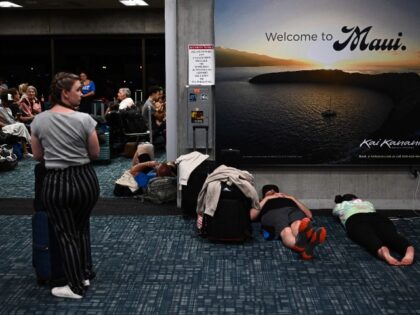 TOPSHOT - Passengers try to sleep below a "Welcome To Maui" billboard on the flo
