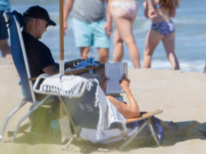 Beachgoers walk along the water as President Joe Biden and first lady Jill Biden sit underneath an umbrella in Rehoboth Beach, Del., Sunday, July 30, 2023. (AP Photo/Manuel Balce Ceneta)