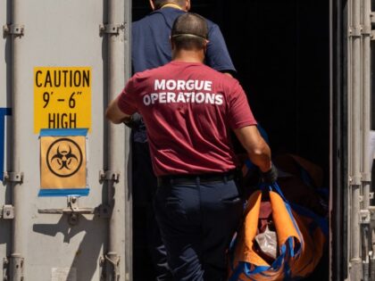 TOPSHOT - Workers wearing "Morgue Operations" shirts move a body bag into a refr