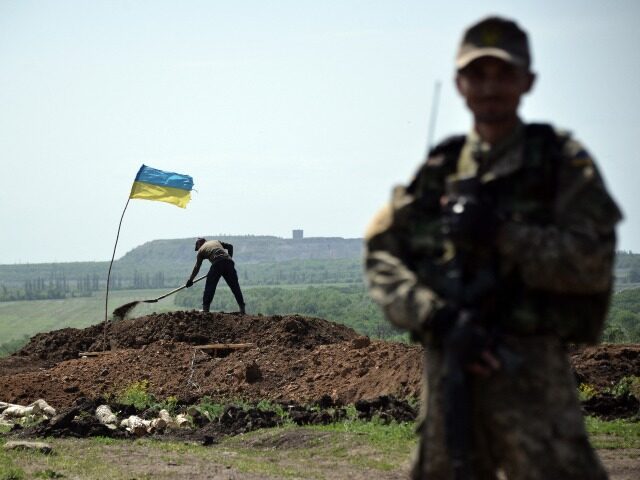 TOPSHOT - An Ukrainian serviceman stands at a position as workers dig trenches on the fron
