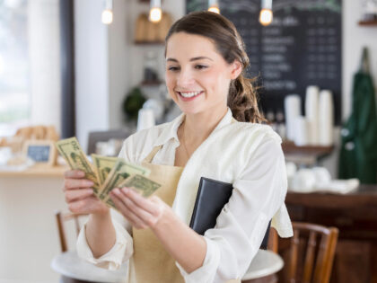 Cheerful young female Hispanic waitress smiles while counting out a large tip.