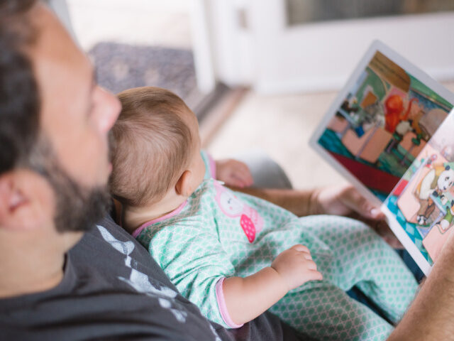 A father sits with his baby and reads to him.