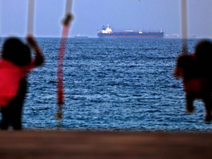Children ride a swing as the Israeli-linked Japanese-owned tanker MT Mercer Street is seen off the port of the Gulf Emirate of Fujairah in the United Arab Emirates on August 3, 2021. - On July 29, two crew members of the tanker MT Mercer Street, managed by a prominent Israeli …