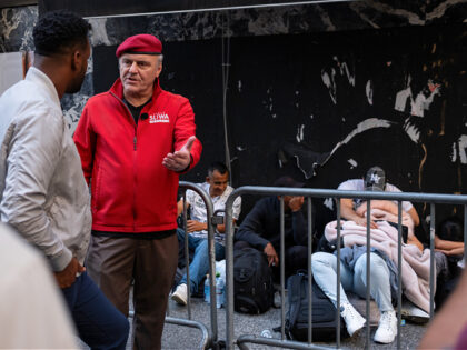 NEW YORK, NEW YORK - AUGUST 02: Curtis Sliwa, former 2022 mayoral candidate and founder of the Guardian Angels, holds an interview while greeting migrants gathered outside of the Roosevelt Hotel where dozens of recently arrived migrants have been camping out as they try to secure temporary housing on August …