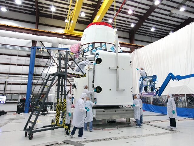 Workers guide a solar array fairing into place inside the processing hangar used by Space