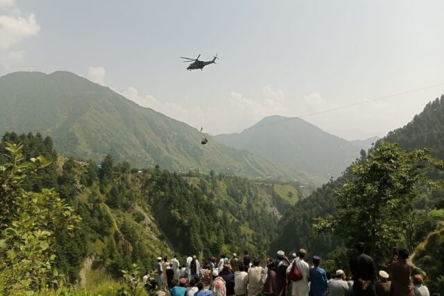 Anxious locals watch as a helicopter flies near the stranded cable car in northern Pakista