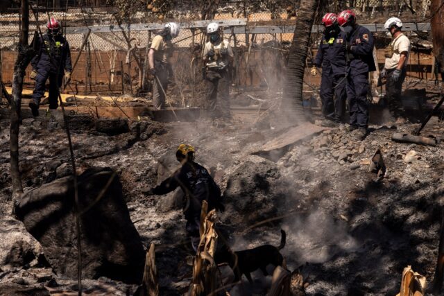 Search and recovery team members check charred buildings and cars in the aftermath of the