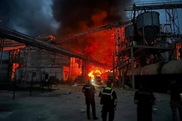 Ukrainian law enforcement officers stand next to the burning industrial facility following