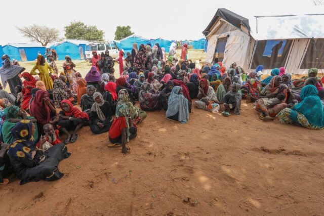 Women who fled the war in Sudan await the distribution of international aid rations at a r