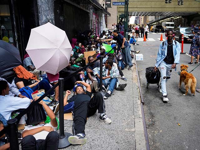 Migrants sit in a queue outside of The Roosevelt Hotel that is being used by the city as t