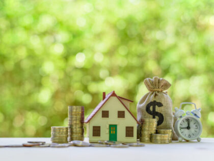 Residential real estate loan, financial concept : House model, coins, US dollar bag, white clock on a table, depicts home loan or borrowing money to buy / purchase a new home for first time homebuyer