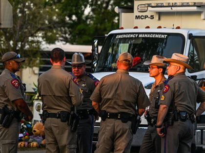 Police officers speak near a makeshift memorial for the shooting victims outside Robb Elementary School in Uvalde, Texas, on May 27, 2022. - Texas police faced angry questions May 26, 2022 over why it took an hour to neutralize the gunman who murdered 19 small children and two teachers in …