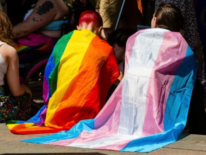 Protesters draped in Rainbow Pride and Transgender flags wait to take part in a London Tra