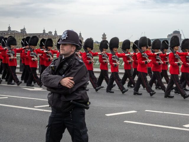 A policeman stands guard as soldiers from the British Army's Grenadier Guard bear the