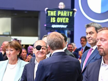 An environmental activist of Greenpeace demonstrates in the background as German Chancellor Olaf Scholz (C-L) and Bavaria's State Premier Markus Soeder arrive at the German car maker BMW booth at the International Motor Show (IAA) in Munich, southern Germany, on September 5, 2023. Germany's IAA MOBILITY auto show, one of …