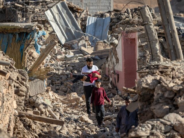 TOPSHOT - People walk past destroyed houses after an earthquake in the mountain village of