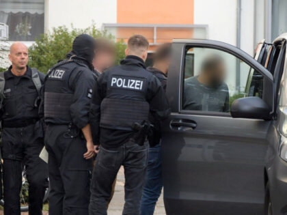 26 September 2023, Bremen: Police officers are on duty during a raid, leading several men to a civilian police vehicle. In a raid in five German states, the federal police discovered several Syrians suspected of having been smuggled in early Tuesday morning. Arrest warrants had also been executed against suspected …
