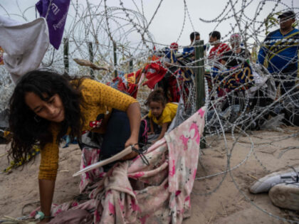 Migrants from Venezuela crawl through a hole in the razor wire to cross into Eagle Pass, T