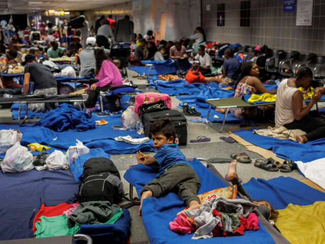 Recently arrived migrants sit on cots and the floor of a makeshift shelter operated by the