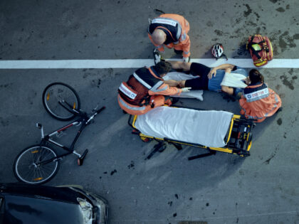 Paramedics raising an injured male cyclist onto stretcher at scene of accident - stock photo