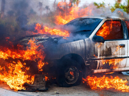 Close-up of burning car after a frontal crash collision on the roadside with flame and smoke.