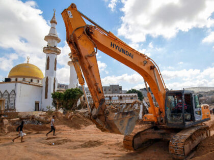 Men walk past a mosque and an earthmover in a flash flood-damaged area in Derna on Septemb