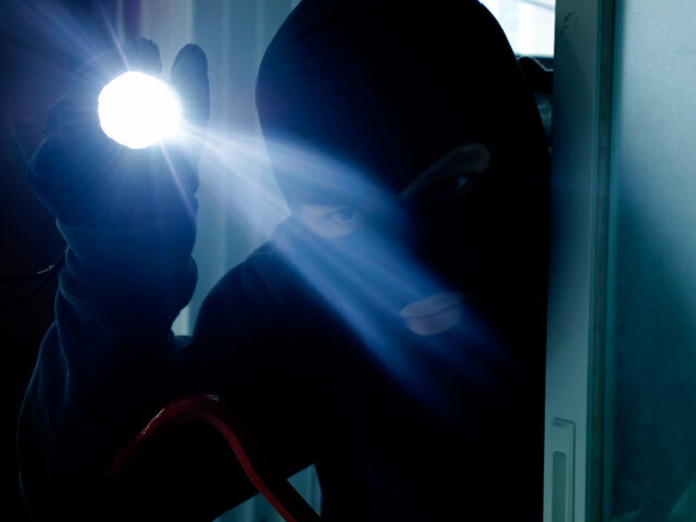 Masked burglar holding flashlight while secretly entering into a house