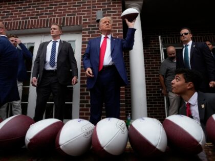 Former President Donald Trump holds a football before throwing it to the crowd during a vi