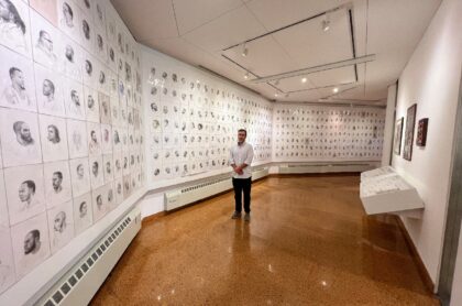 Artist Mark Loughney stands in front of his piece "Pyrrhic Defeat: A Visual Study of Mass Incarceration," displaying hundreds of portraits of incarcerated men he made while in prison himself