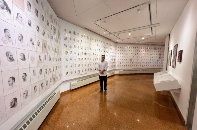 Artist Mark Loughney stands in front of his piece "Pyrrhic Defeat: A Visual Study of Mass