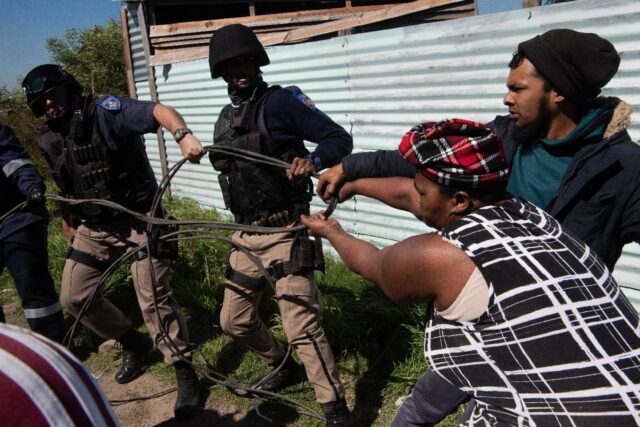 Cape Town police try to prise an illegally connected electricity cable from residents of a