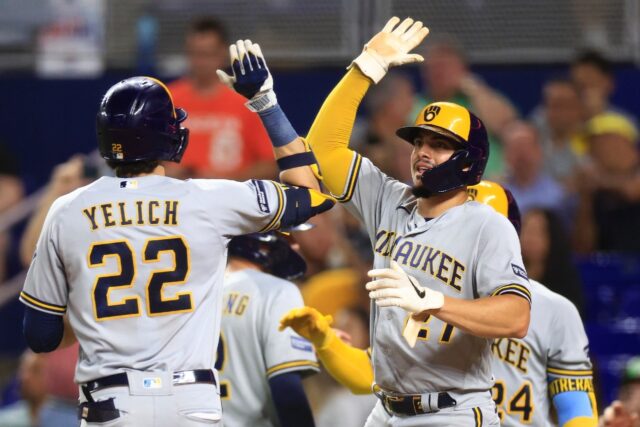 Christian Yelich high fives Milwaukee Brewers teammate Willy Adames after hitting a three-