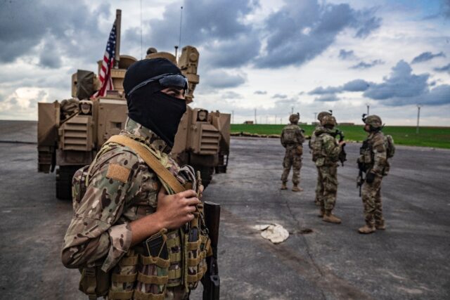 A member of the Syrian Democratic Forces and US soldiers are pictured on the outskirts of