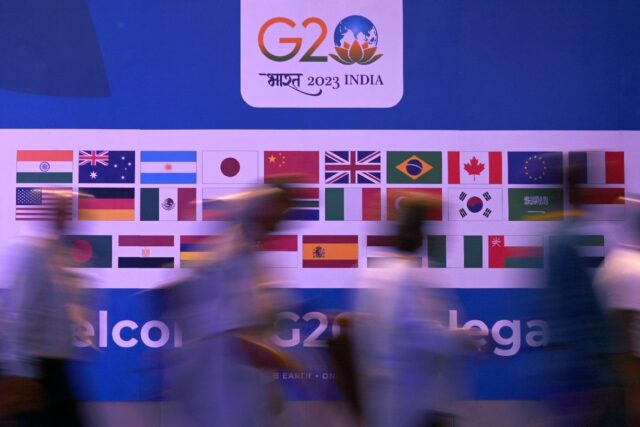 People walk past a banner with flags of countries participating in the G20 summit in New D
