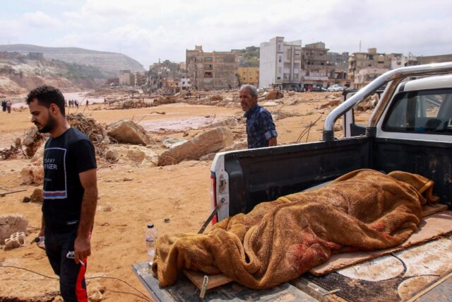 People walk past the body of a victim from the flood which devastated Derna, eastern Libya