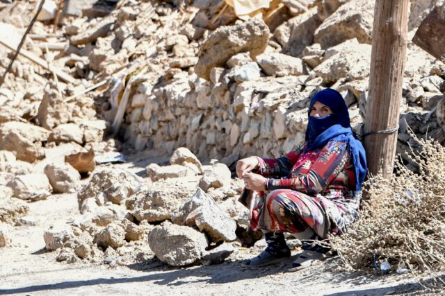 A woman sits near debris from destroyed buildings in the earthquake-hit village of Ardouz