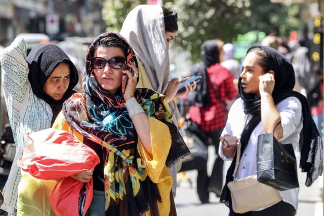 A woman speaks on a mobile phone while walking along a street in Tehran