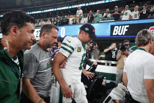 New York Jets quarterback Aaron Rodgers, wearing a cap as he is helped off the field after