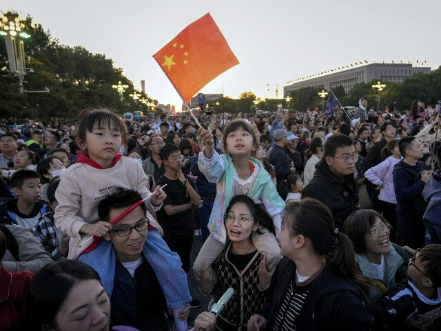 A child waves a national flag as visitors gather on a street near Tiananmen Square to watc