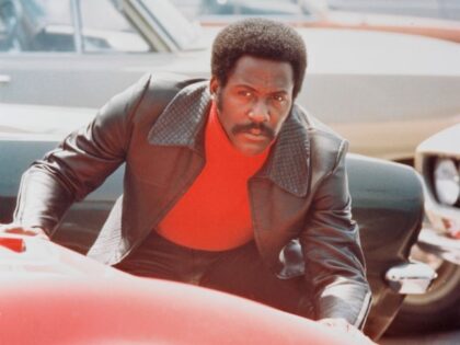 Richard Roundtree, US actor, crouching behind a red sports car in a publicity still issued